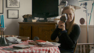 Woman at dining room table with camera - scene from Sarah Polley's Stories We Tell